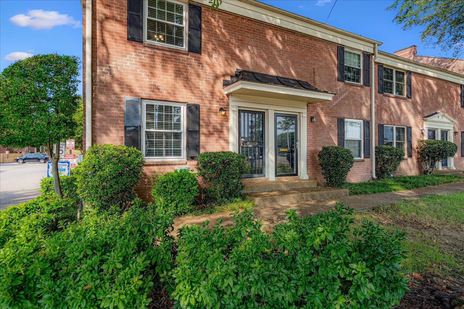 a view of a brick house with a yard plants and large tree