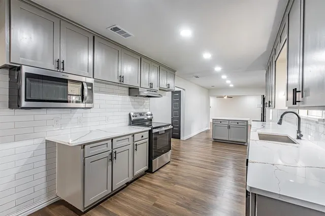 a kitchen with stainless steel appliances granite countertop a sink a stove top oven and wooden floor