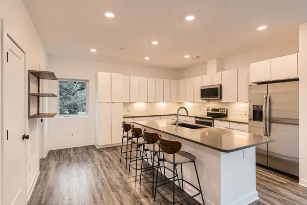 a kitchen with stainless steel appliances granite countertop a refrigerator a sink dishwasher a stove and white cabinets with wooden floor