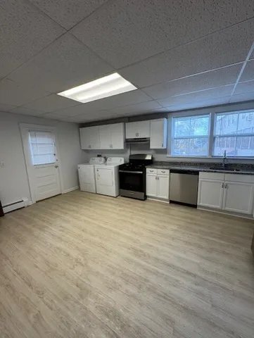 a large kitchen with stainless steel appliances granite countertop a stove a sink dishwasher and white cabinets with wooden floor