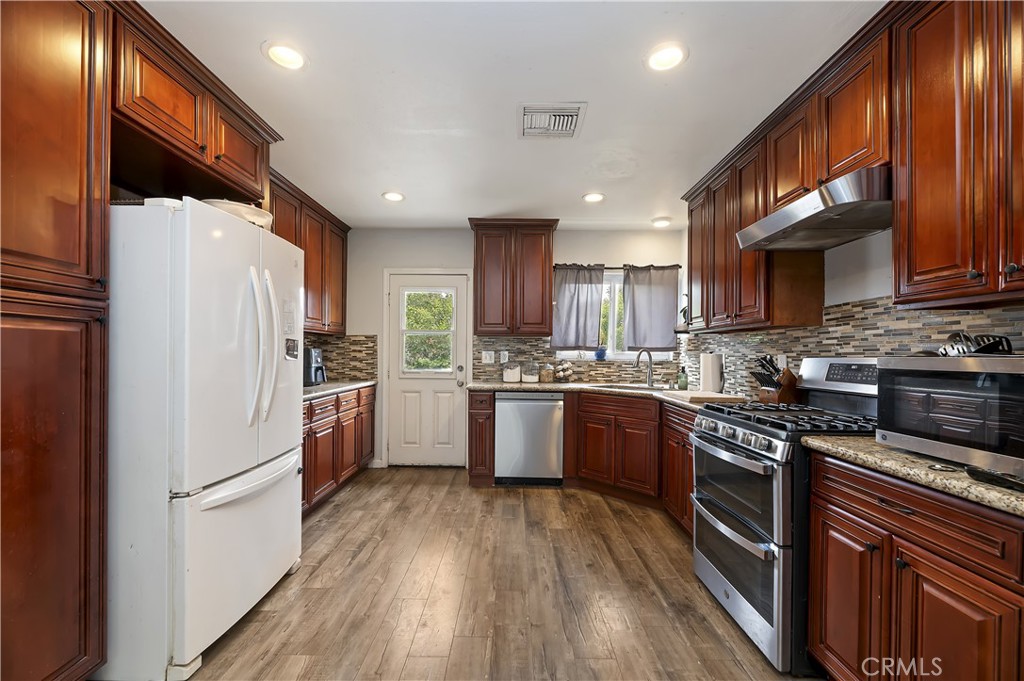 3075 Ronald Street Riverside, CA 92506 - Photo 12 of 30 a kitchen with granite countertop a refrigerator a sink dishwasher a stove top oven a kitchen island and cabinets with wooden floor
