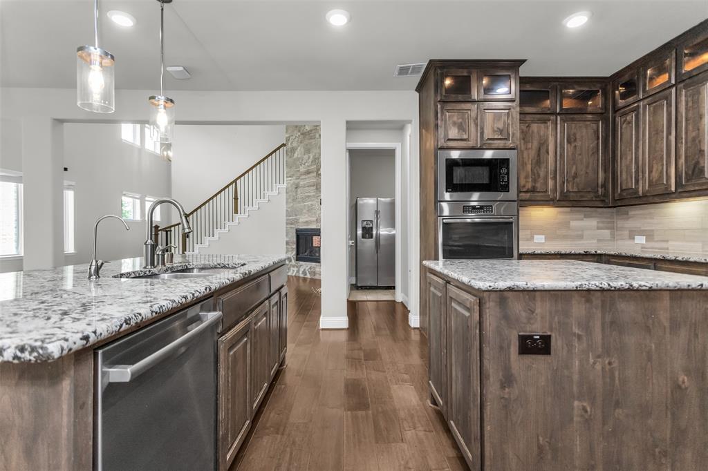 6333 Hall Road Frisco, TX 75034 - Photo 17 of 38 Gourmet kitchen featuring granite countertops, wood-finish flooring, custom cabinetry, stainless steel appliances, and a stone fireplace surround