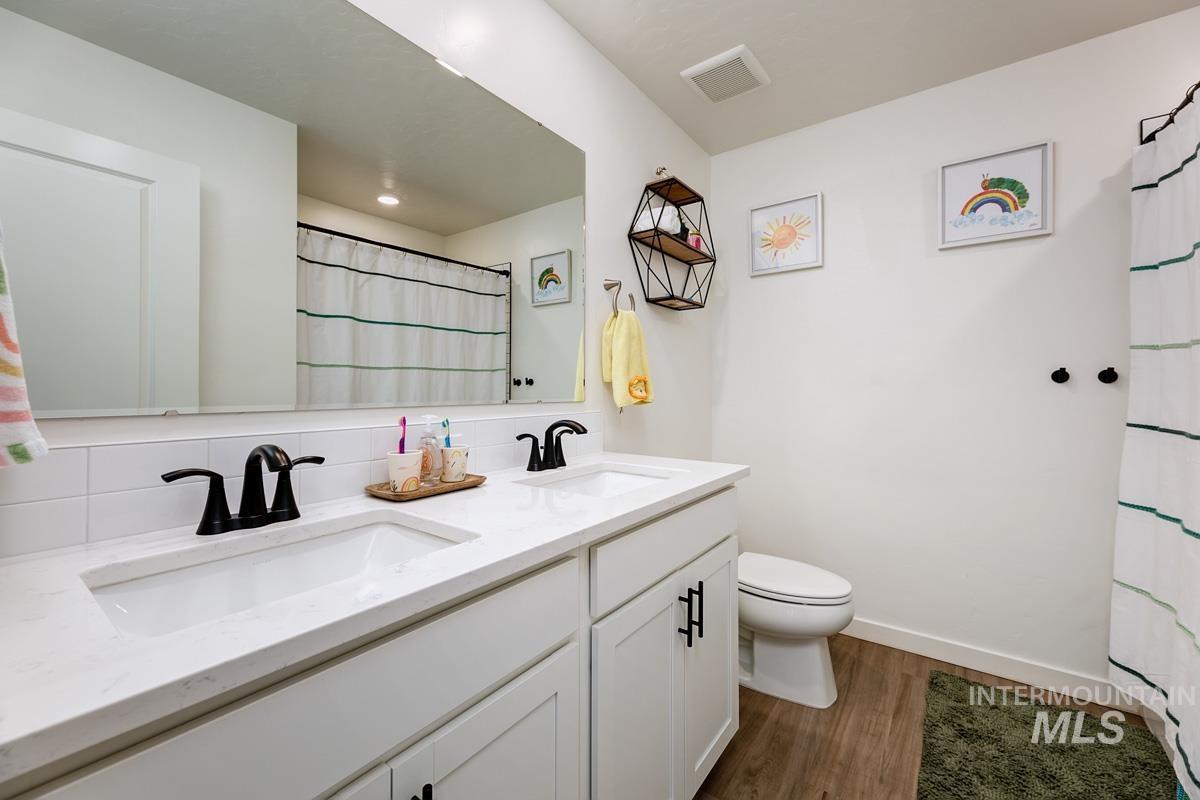 4469 South Colditz Way Meridian, ID 83642 - Photo 23 of 30 Bathroom featuring a dual vanity with white cabinetry and integrated sinks, a white subway tile backsplash, and dark bronze fixtures