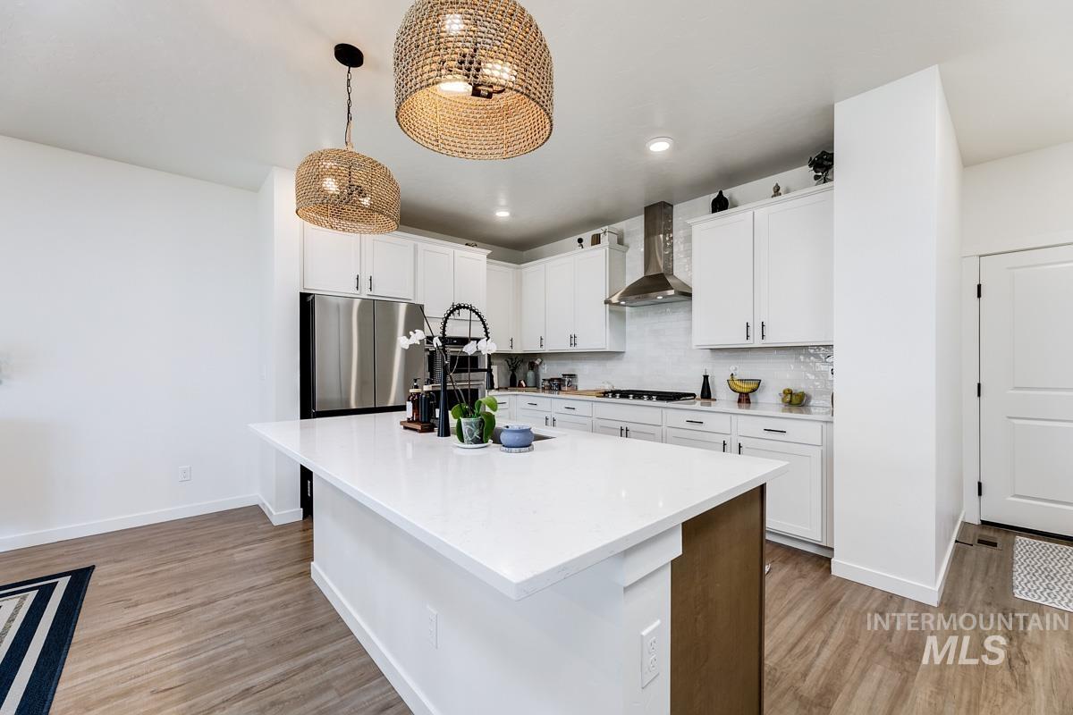 4469 South Colditz Way Meridian, ID 83642 - Photo 5 of 30 Modern kitchen featuring a large central island with a white countertop, white cabinetry with dark hardware, stainless steel appliances, and wood-finish flooring