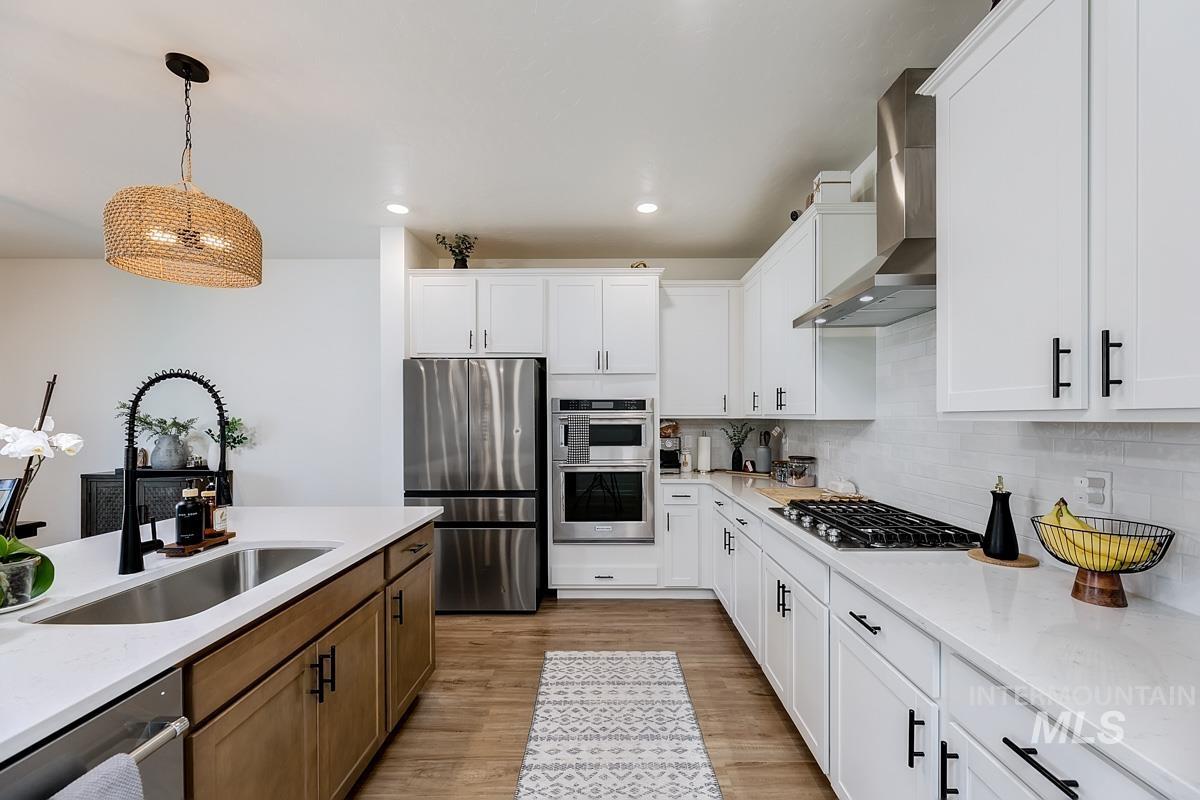 4469 South Colditz Way Meridian, ID 83642 - Photo 6 of 30 Contemporary kitchen featuring white cabinetry, stainless steel appliances, a gas cooktop with a range hood, an island with a built-in sink, and wood-finish flooring