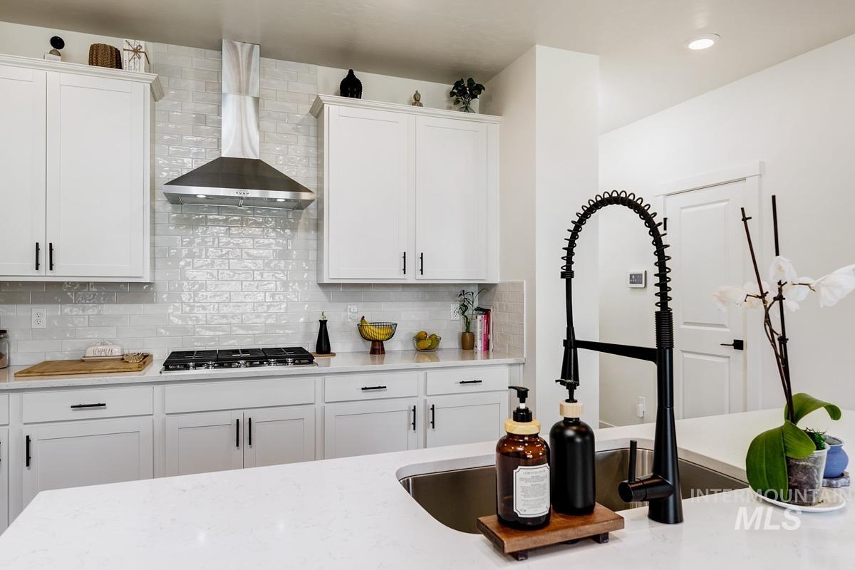 4469 South Colditz Way Meridian, ID 83642 - Photo 7 of 30 White cabinetry kitchen featuring a gas cooktop, stainless steel range hood, subway tile backsplash, and light-toned countertops