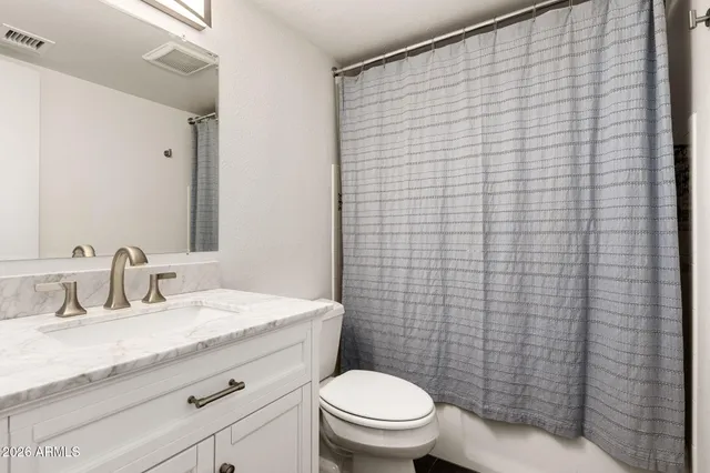 a bathroom with a granite countertop toilet a sink a mirror and a shower