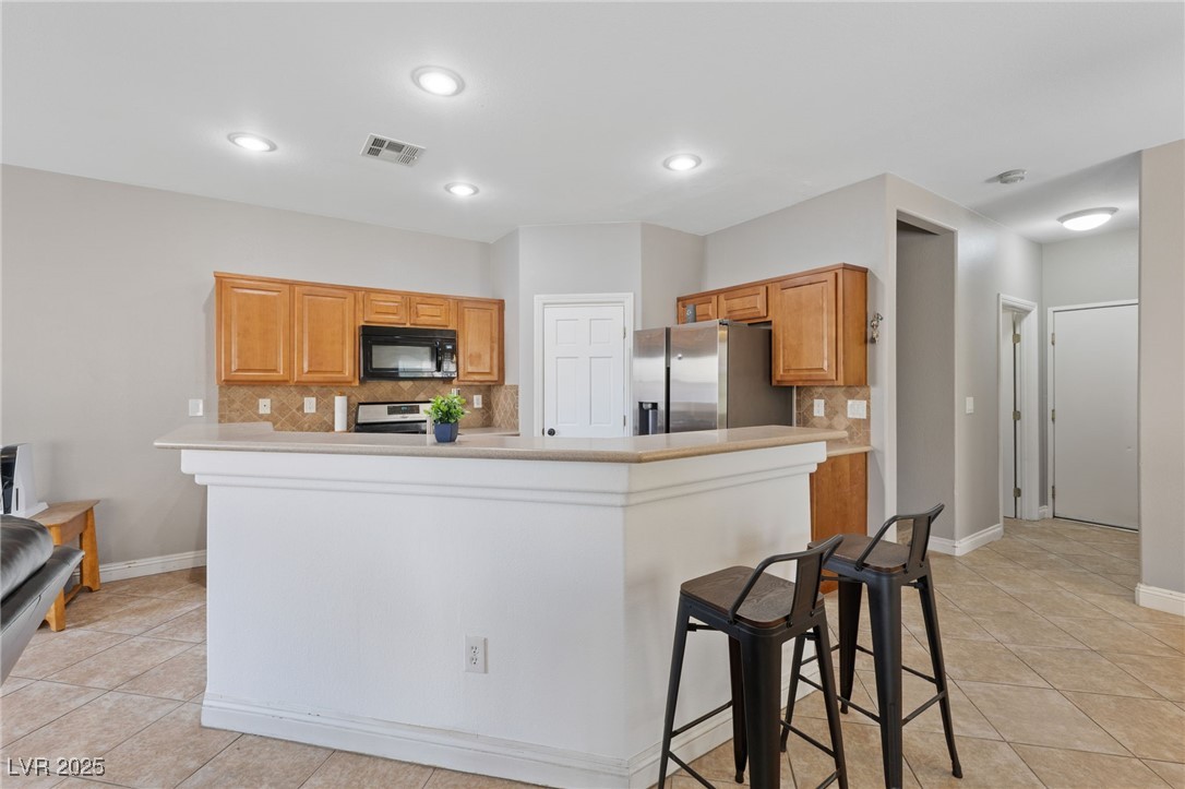 9068 Bushy Tail Avenue, Unit 103 Las Vegas, NV 89149 - Photo 2 of 32 Kitchen with light countertops, pantry, stainless steel appliances, maple cabinets, a breakfast bar, and recessed lighting