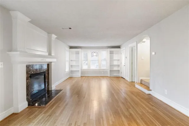 a view of an empty room with wooden floor fireplace and a window