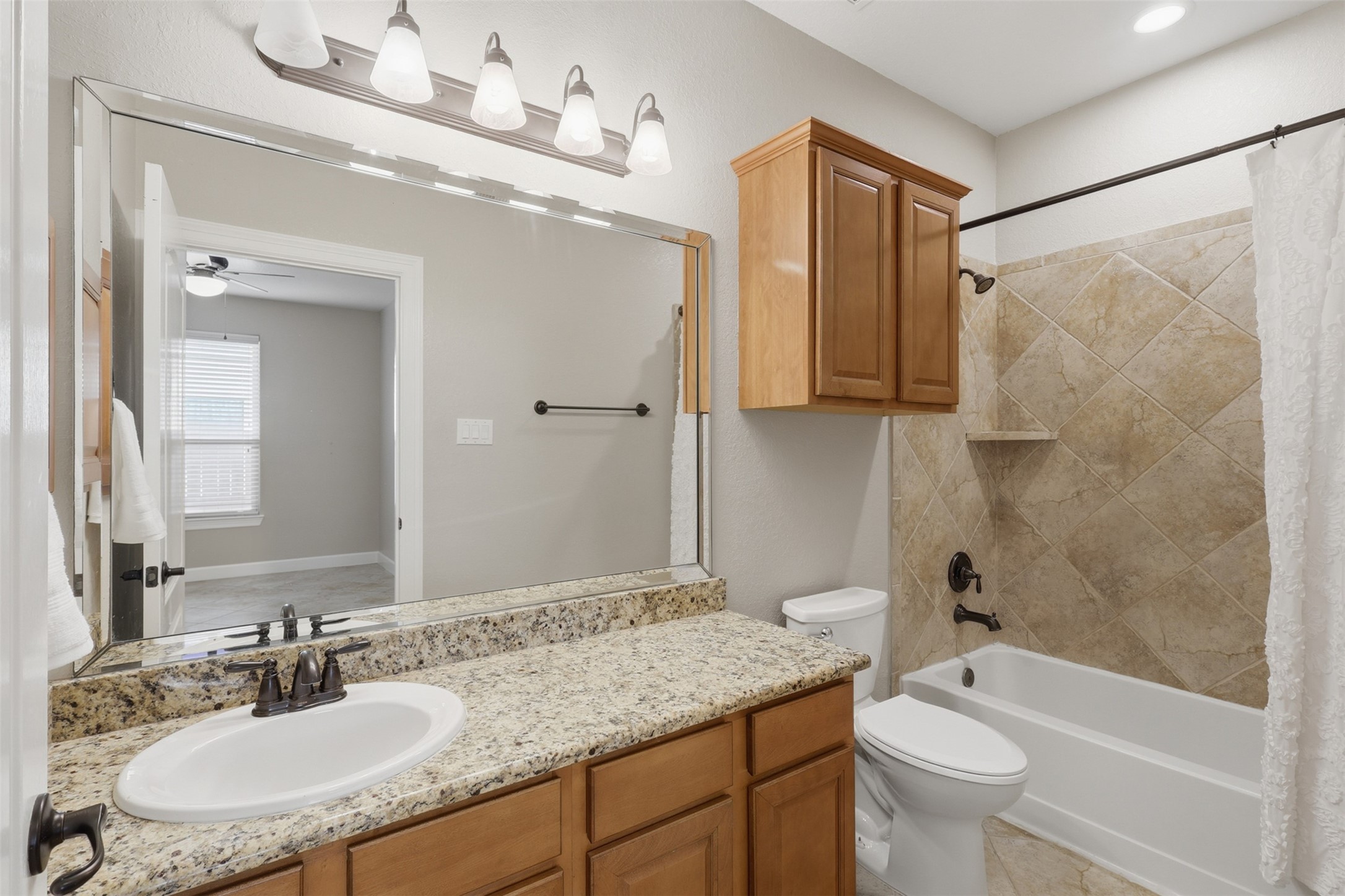 721 Rufina Street League City, TX 77573 - Photo 18 of 33 Beautifully appointed with granite countertops, warm wood cabinetry, updated fixtures, and a large mirror, the secondary bath offers both style and everyday functionality. The tiled tub and shower surround provides a timeless finish that's easy to maintain.