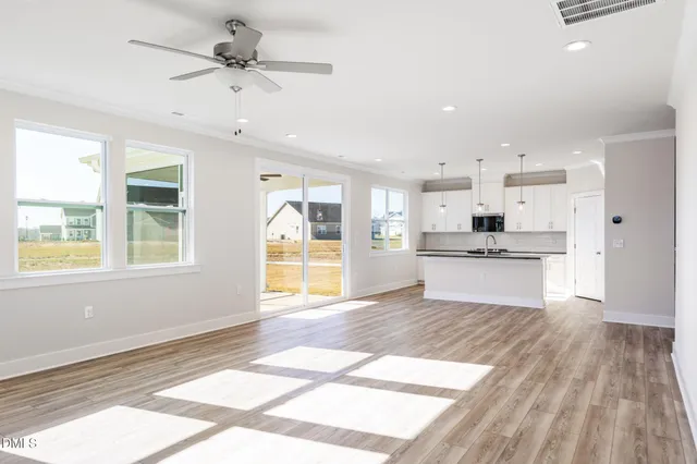 an empty room with wooden floor chandelier fan and windows
