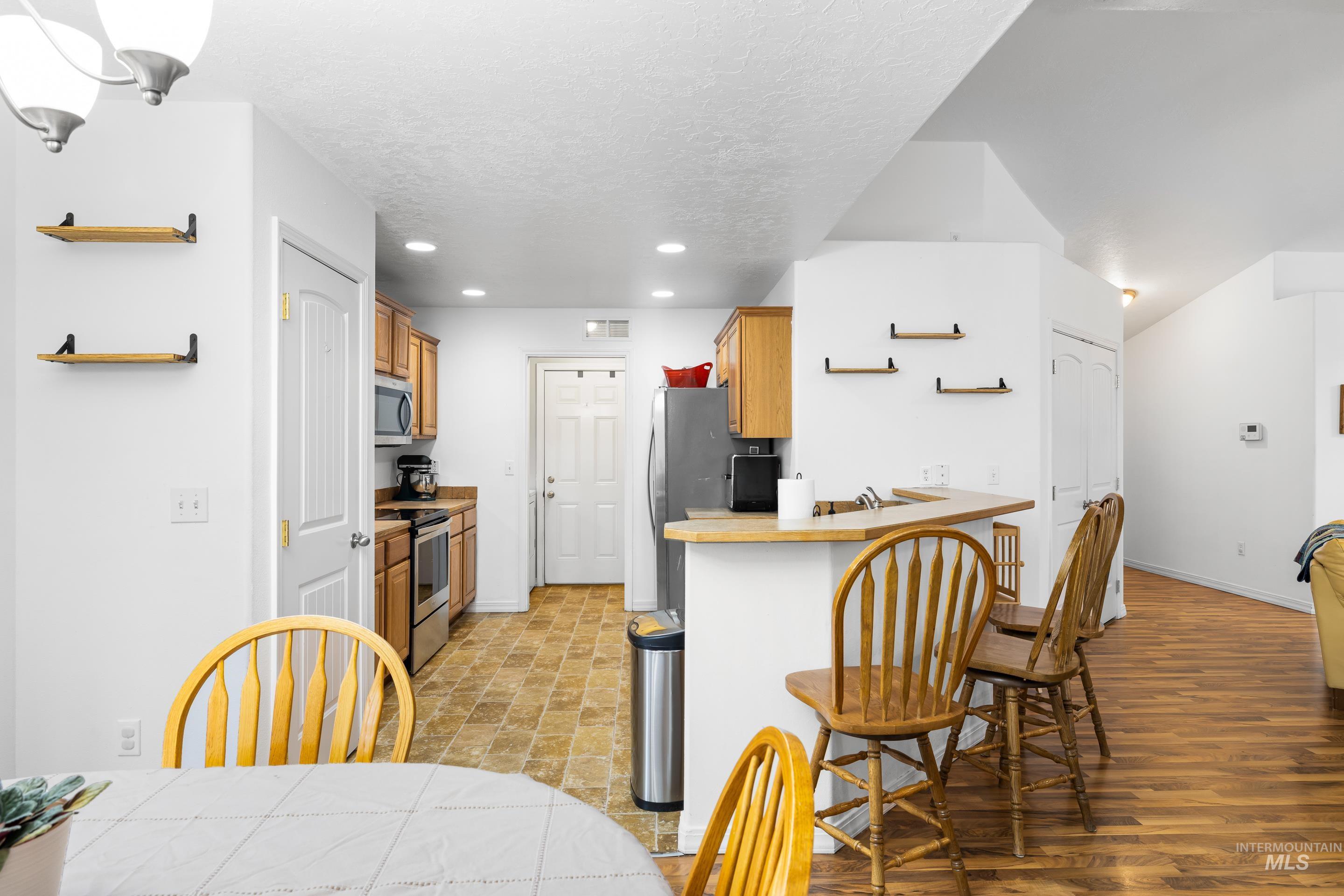 191 Southwest Quaker Drive Mountain Home, ID 83647 - Photo 15 of 43 Kitchen with open shelves, brown cabinetry, light countertops, a textured ceiling, and appliances with stainless steel finishes