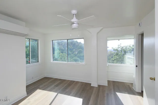 an empty room with wooden floor fan and windows