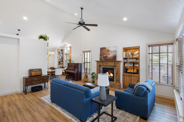 882 Sego Lily Way Mapleton, UT 84664 - Photo 5 of 41 Spacious living area featuring a vaulted ceiling with a ceiling fan, wood-finish flooring, a fireplace with a wood mantel, built-in shelving, and large windows with blinds