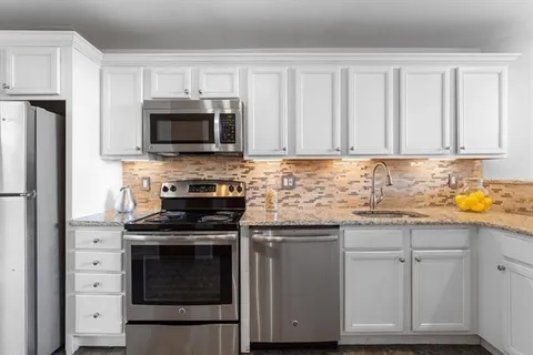 a kitchen with granite countertop white cabinets and stainless steel appliances