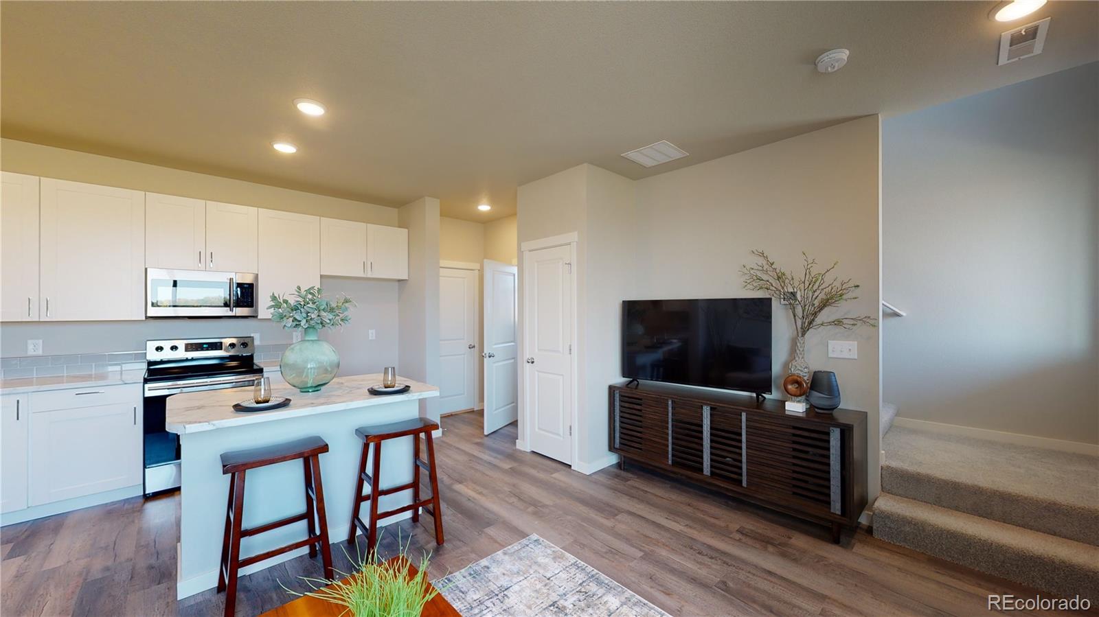 1353 Reynolds Street, Unit 9B Fort Lupton, CO 80621 - Photo 5 of 14 a kitchen with stainless steel appliances a stove a refrigerator and a dining table with wooden floor