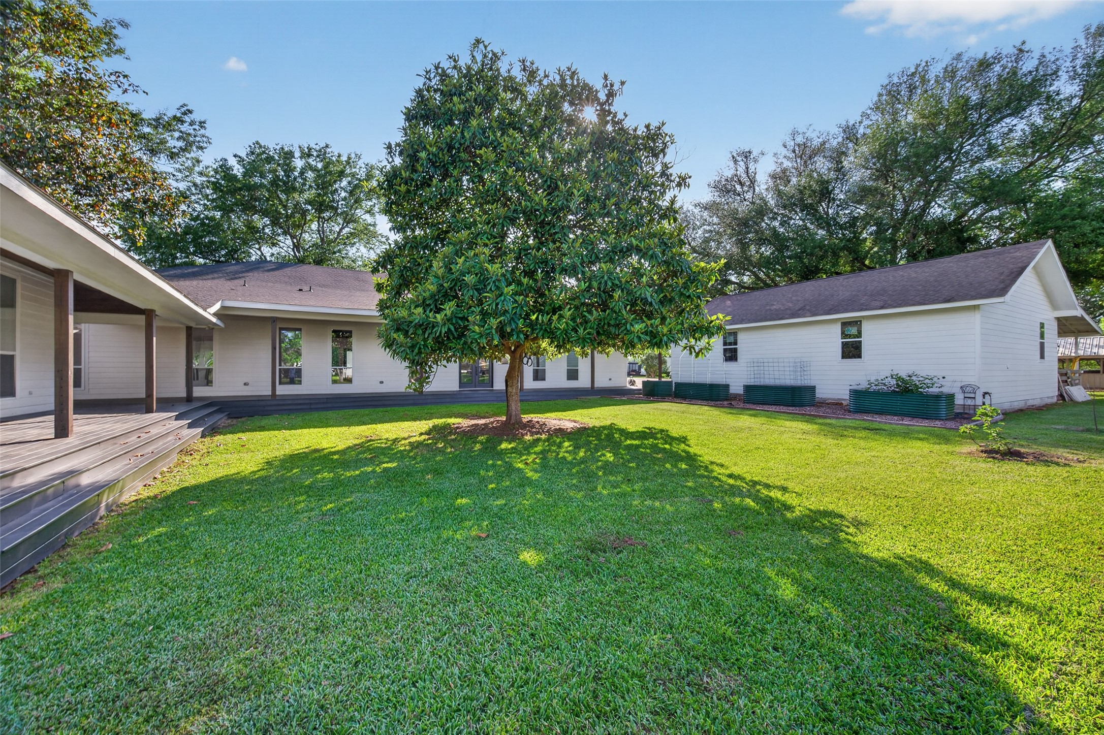 12625 Padon Road Needville, TX 77461 - Photo 42 of 50 Main home thoughtfully positioned between the private guest house and spacious barn, all connected by a large wooden deck. Expansive green lawn at the center creates a peaceful outdoor living space, complemented by raised garden beds—perfect for homestead living and multi-generational flexibility.