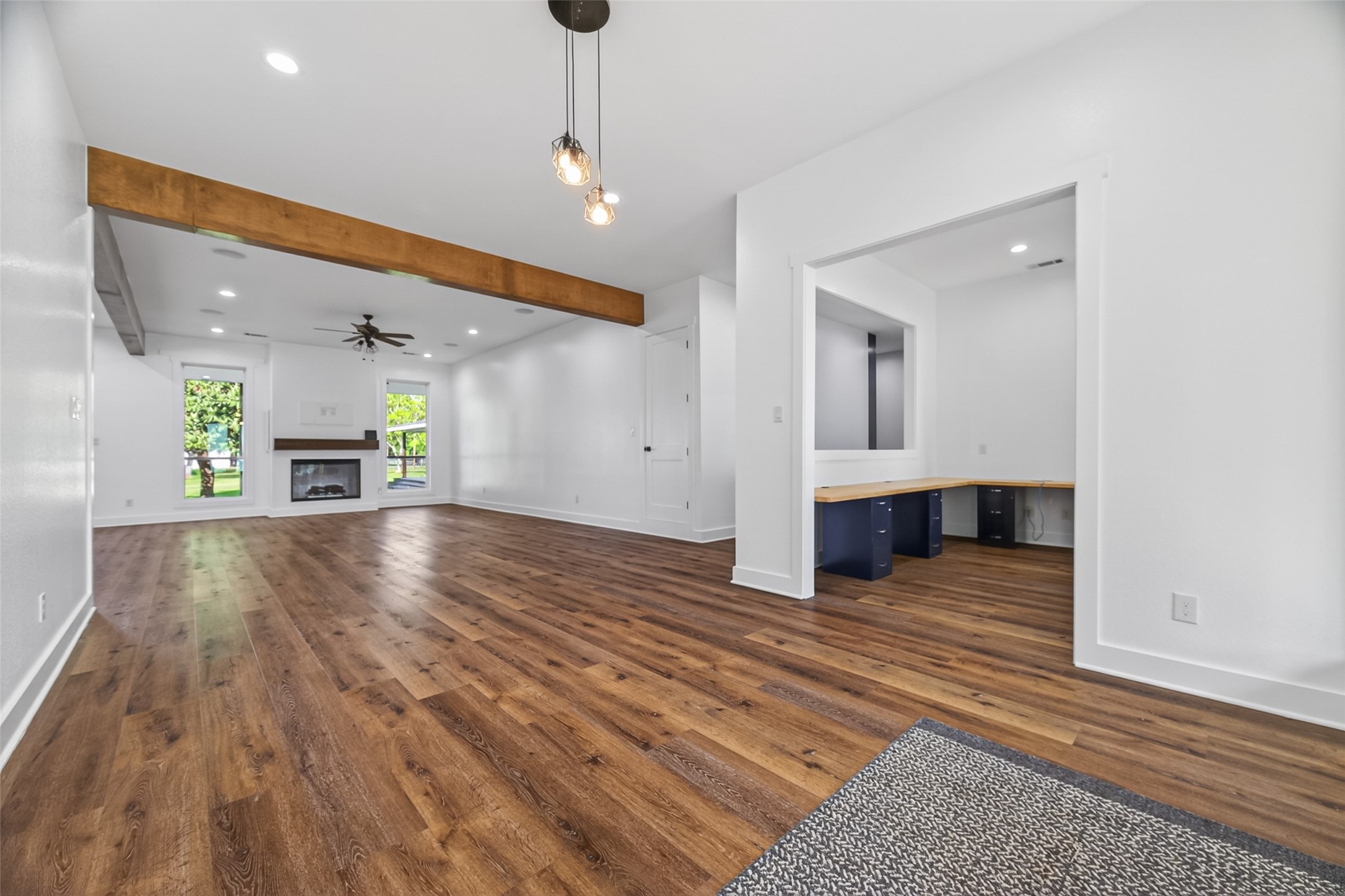 12625 Padon Road Needville, TX 77461 - Photo 5 of 50 Spacious open-concept living area with warm wood flooring, exposed beam detail, fireplace, and dedicated workspace—ideal for both everyday living and entertaining.