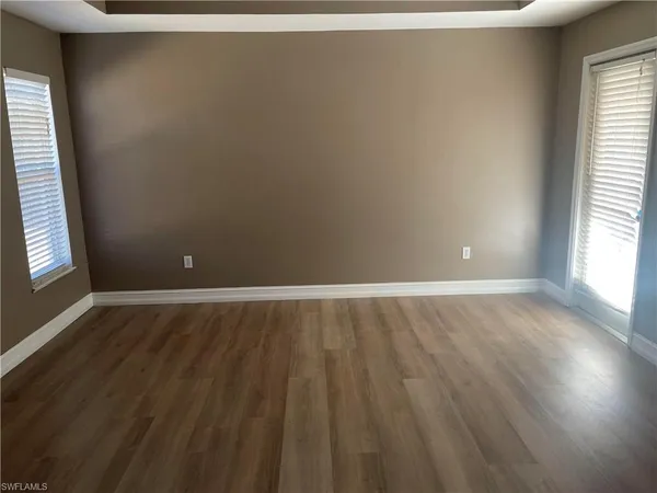 an empty room with wooden floor and windows with curtains