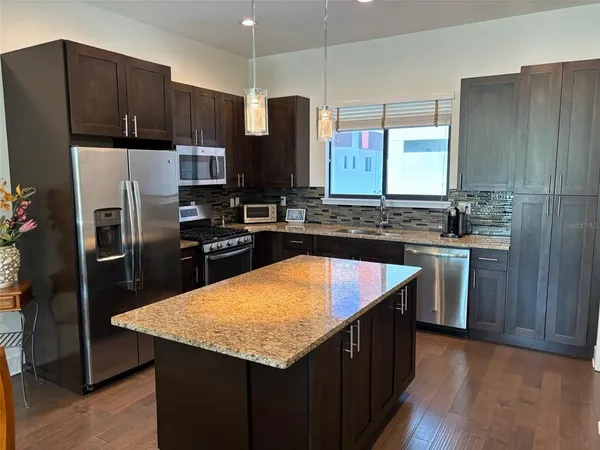 a kitchen with kitchen island granite countertop wooden cabinets a refrigerator a sink and dishwasher with wooden floor