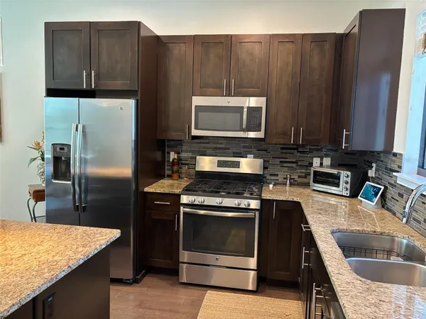 a kitchen with granite countertop wooden cabinets a stove and a refrigerator with wooden floor