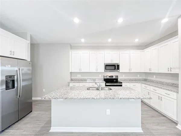 a kitchen with granite countertop a stove top oven a sink a refrigerator and white cabinets