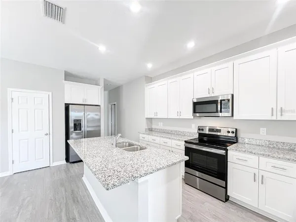 a kitchen with stainless steel appliances granite countertop a stove top oven a sink dishwasher and a refrigerator with wooden floor