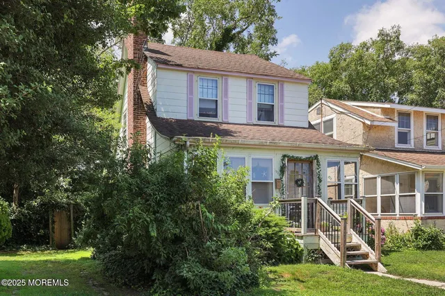 a view of a house with brick walls and a yard with plants and large trees