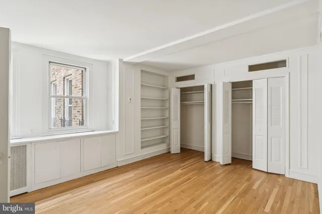 an empty room with wooden floor closet and windows