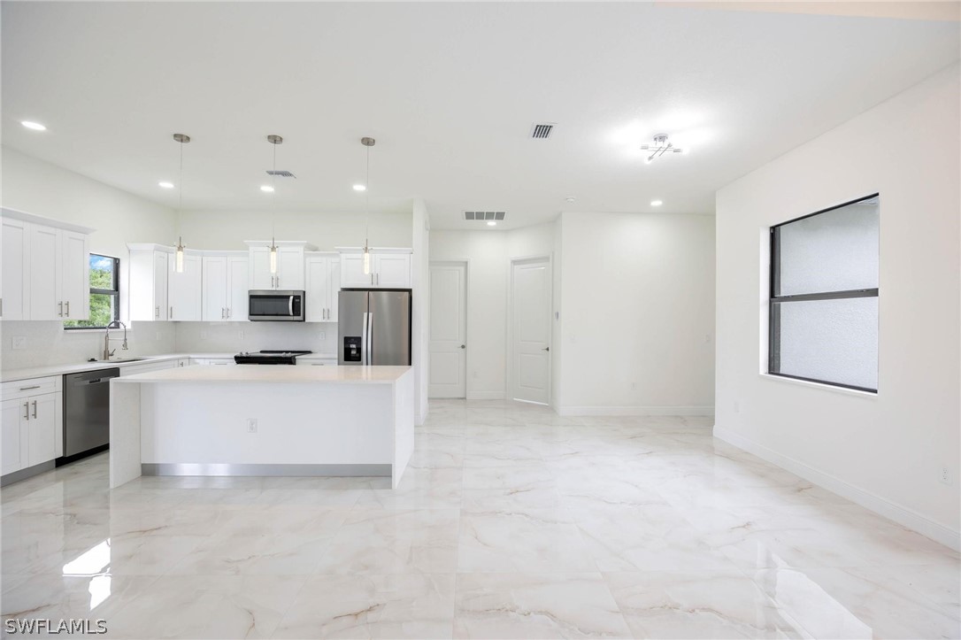 2909 37th Street Southwest Lehigh Acres, FL 33976 - Photo 25 of 29 a large white kitchen with kitchen island a stove a sink a refrigerator and white cabinets with wooden floor