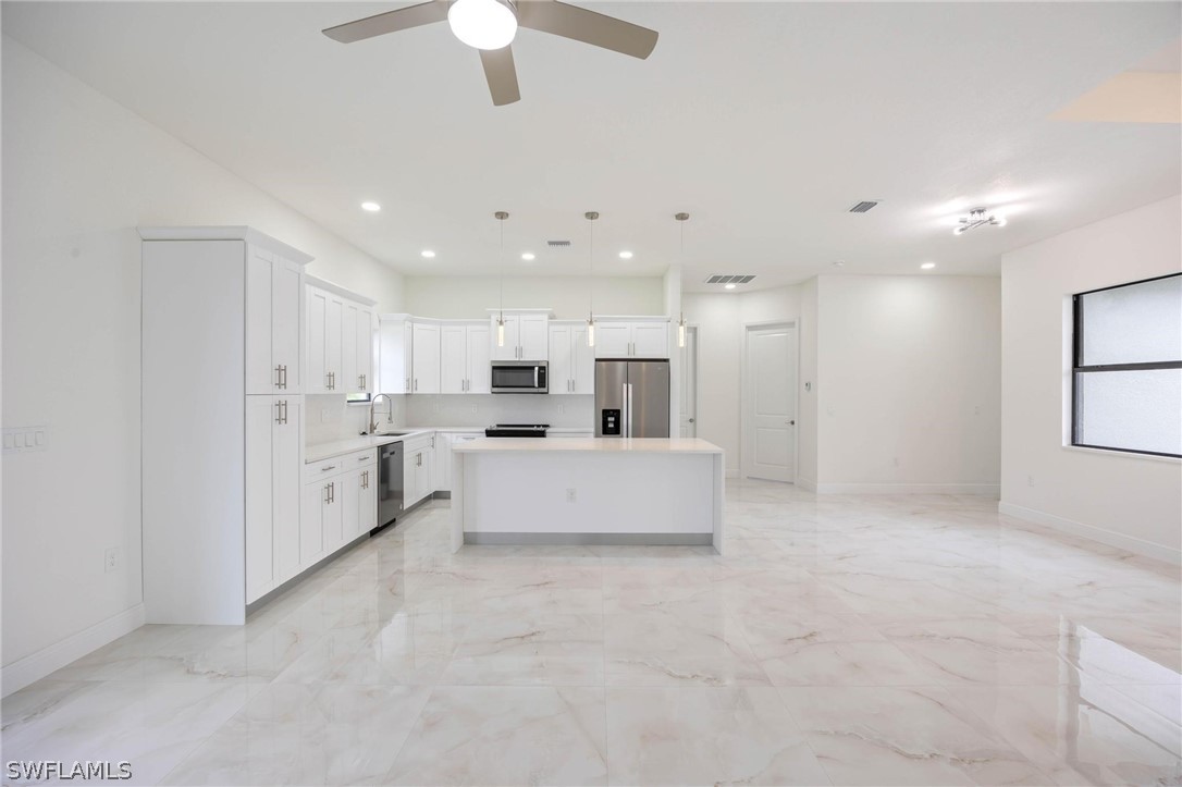 2909 37th Street Southwest Lehigh Acres, FL 33976 - Photo 5 of 29 a large white kitchen with kitchen island a stove a sink a refrigerator and white cabinets