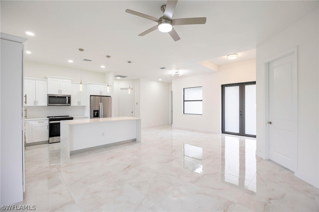 2909 37th Street Southwest Lehigh Acres, FL 33976 - Photo 6 of 29 a large white kitchen with kitchen island a stove a sink a refrigerator and white cabinets with wooden floor