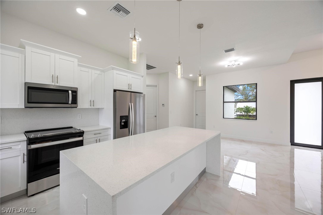 2909 37th Street Southwest Lehigh Acres, FL 33976 - Photo 9 of 29 a large white kitchen with kitchen island a sink a stove and refrigerator