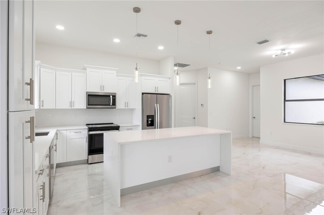 2909 37th Street Southwest Lehigh Acres, FL 33976 - Photo 10 of 29 a large white kitchen with stainless steel appliances a stove a refrigerator a sink and white cabinets