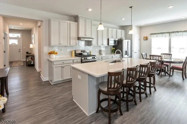 a kitchen with stainless steel appliances granite countertop a stove a refrigerator a kitchen island a dining table and chairs with wooden floor
