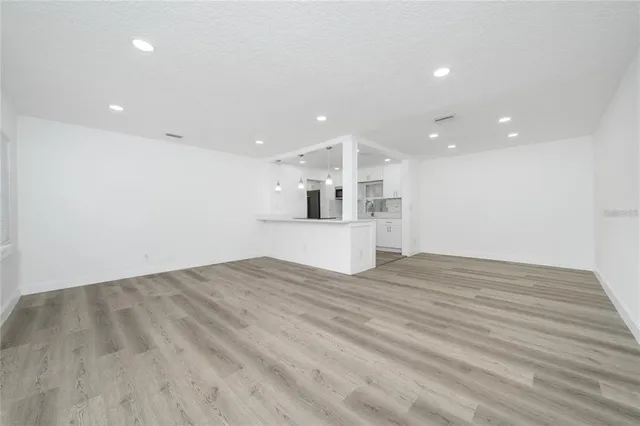 a view of empty room with wooden floor and kitchen