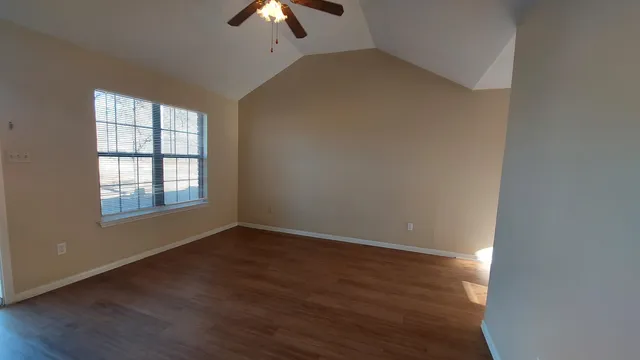 an empty room with wooden floor chandelier fan and windows