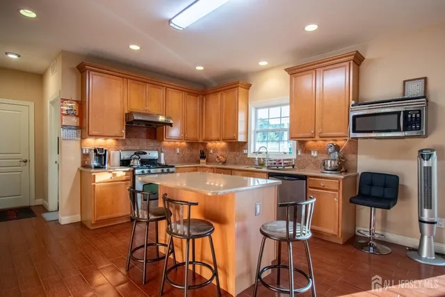 a kitchen with stainless steel appliances granite countertop a stove top oven a refrigerator a sink and a dining table with wooden floor