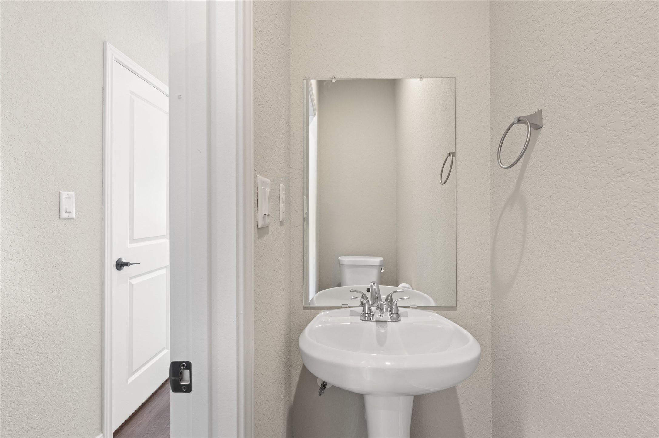 14010 Longstreet Road, Unit 2 Willis, TX 77318 - Photo 25 of 29 This photo shows a small, well-lit powder room with a pedestal sink, a mirror, and a toilet. The walls are painted a neutral color, and there’s a towel ring next to the sink.