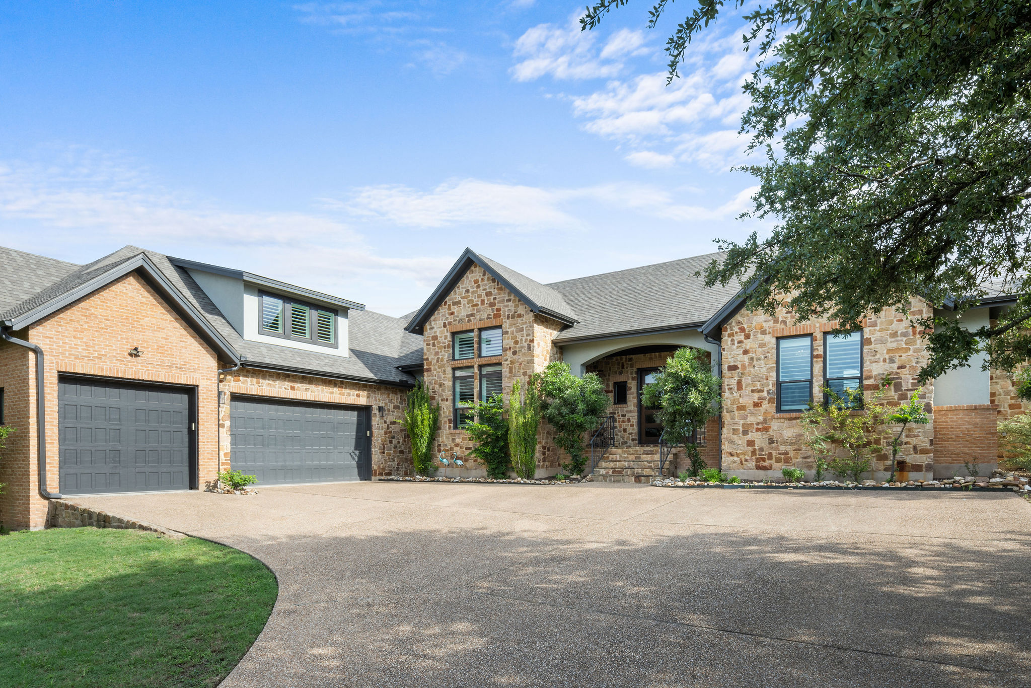 View of front of home featuring a shingled roof, stone siding, and concrete driveway
