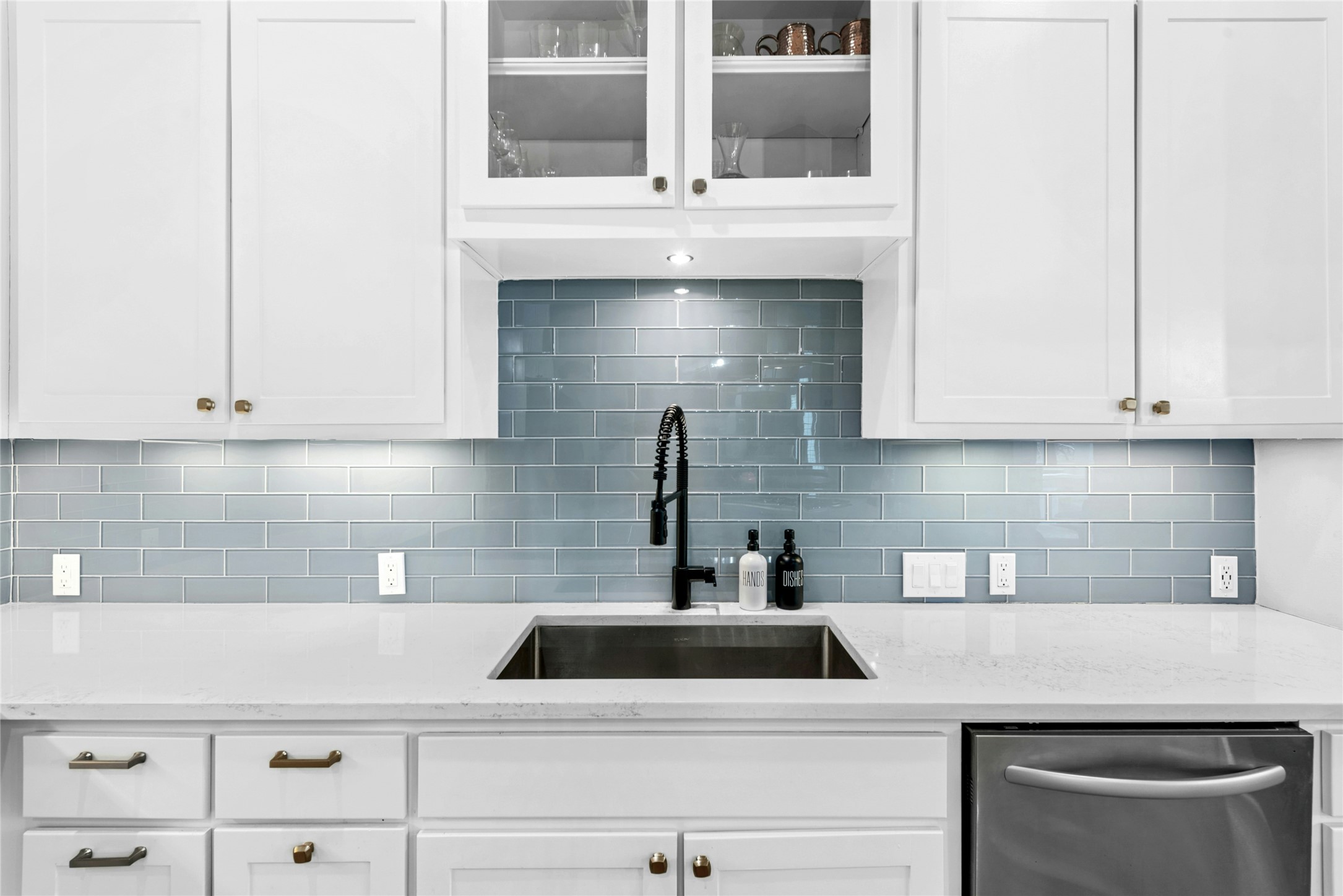 279 Rugged Earth Drive Austin, TX 78737 - Photo 18 of 40 Kitchen featuring glass insert cabinets, light stone countertops, stainless steel dishwasher, white cabinetry, and backsplash