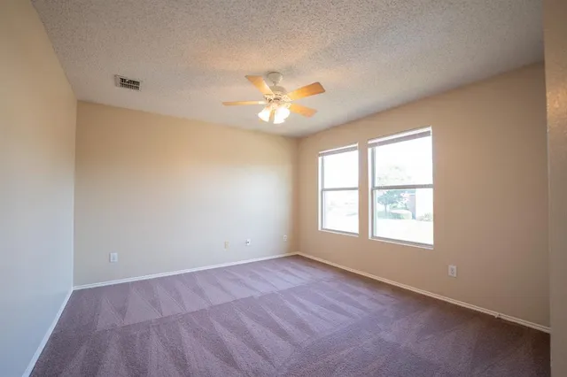 an empty room with chandelier fan and windows
