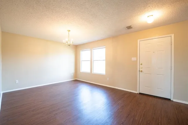 an empty room with wooden floor chandelier and windows