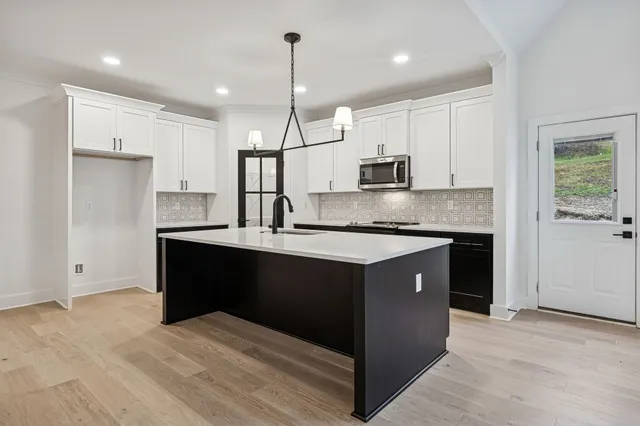 a kitchen with kitchen island granite countertop a refrigerator a sink dishwasher a stove and white cabinets with wooden floor