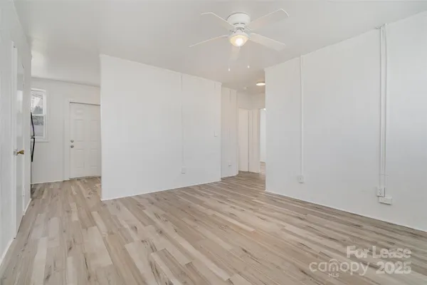 a view of an empty room with wooden floor and a ceiling fan