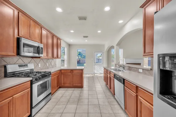 a large kitchen with stainless steel appliances granite countertop a stove top oven a sink dishwasher a dining table and chairs with wooden cabinets