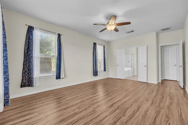 a view of an empty room with wooden floor and a ceiling fan