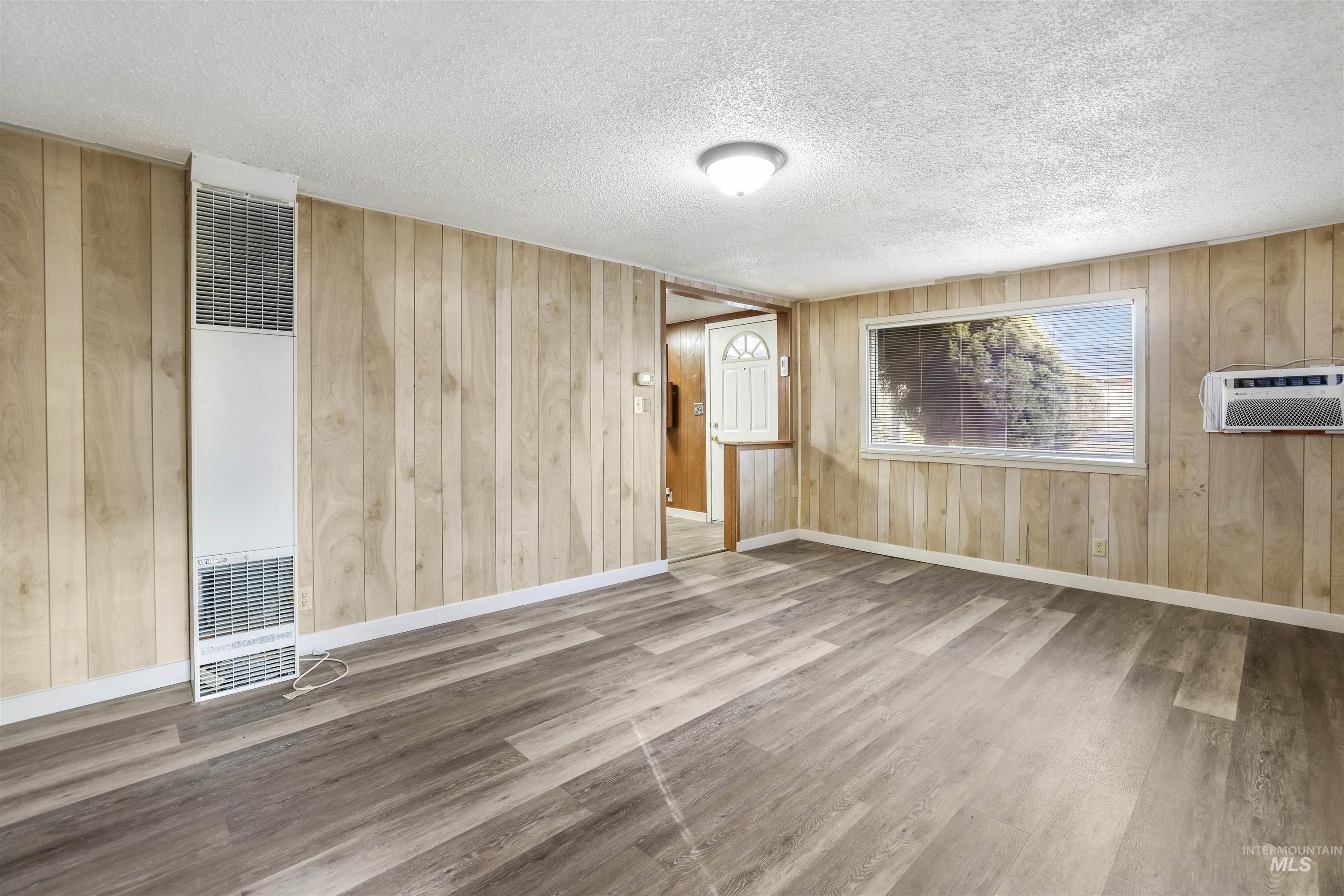 545 Madison Street Twin Falls, ID 83301 - Photo 11 of 23 Empty room featuring wood walls, wood finished floors, a textured ceiling, a heating unit, and an AC wall unit