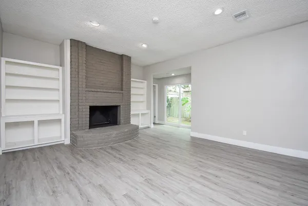 an empty room with wooden floor fireplace and windows