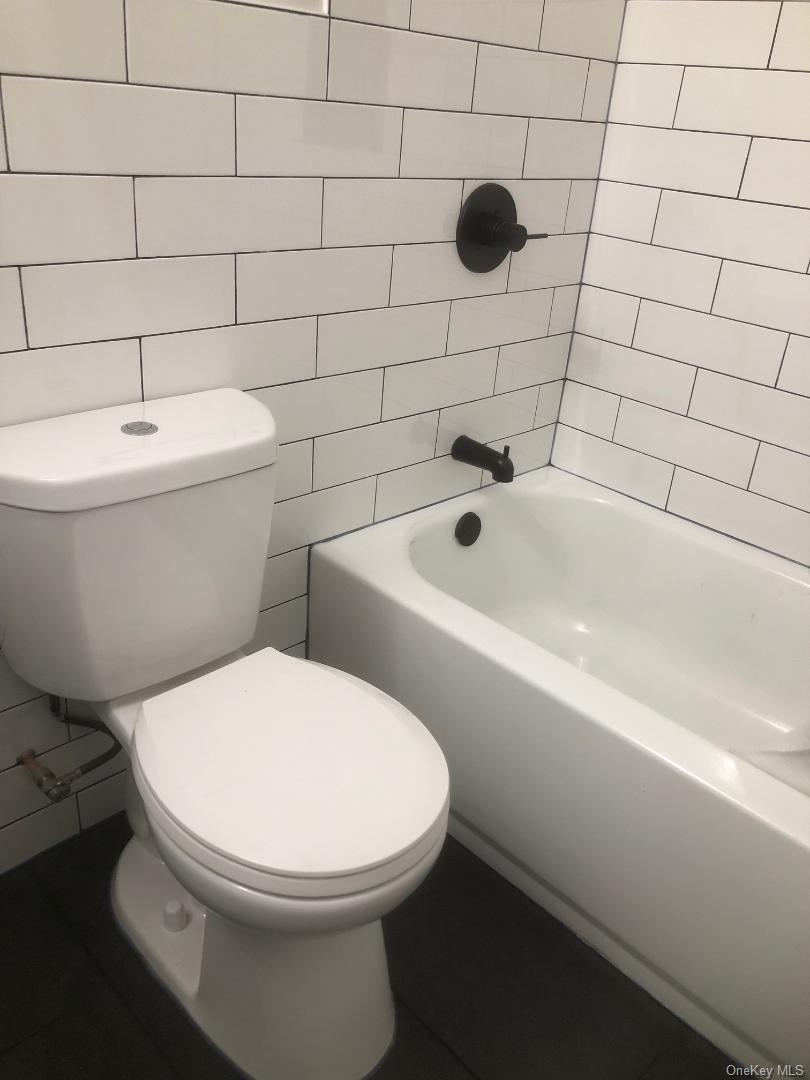 85 North Middletown Road, Unit A7 Nanuet, NY 10954 - Photo 11 of 12 Bathroom featuring a shower/tub combination, white subway tile walls, a standard white toilet, a white bathtub, dark floor tiling, and matte black fixtures